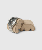 A silver wristwatch with a black dial elegantly sits on TAWBURY's Grove Watch Box Pillow, X-Small, in beige, designed for any wrist size, against a plain gray background.